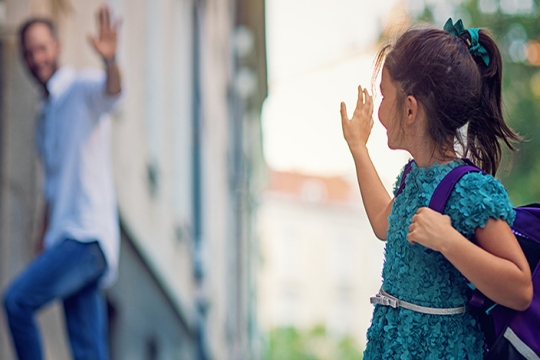 Girl in blue dress waves goodbye to a man